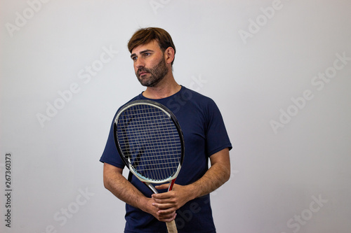 Portrait of handsome young man playing tennis holding a racket with brown hair looking melancholy, facing forwards and looking at the horizon. Isolated on white background. © Sergio Barceló