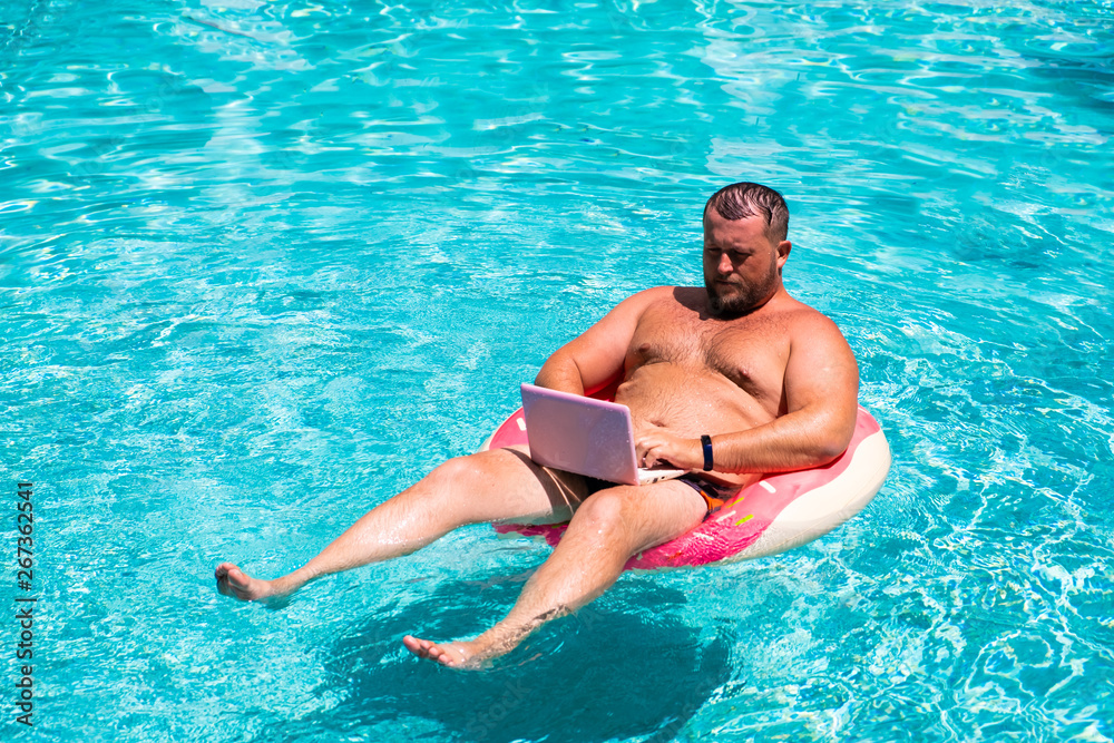 Male businessman with an inflatable ring in the water in the pool. Funny Fat Man in Swimming Circle with Pink Laptop. freelance concept.