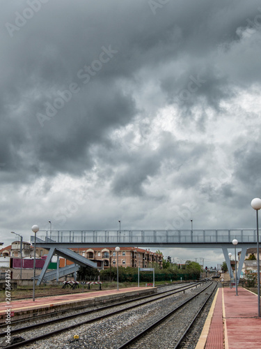 Train tracks and pedestrian bridge in the background with a sky of storm clouds in the station of Torrijos, province of Toledo. Castilla la Mancha. Spain