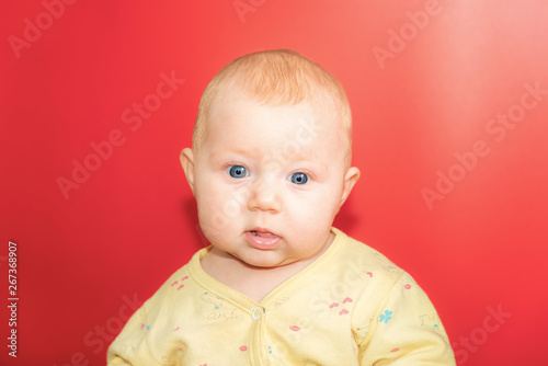 Portrait of a baby on a red background, newborn girl close-up in the studio.
