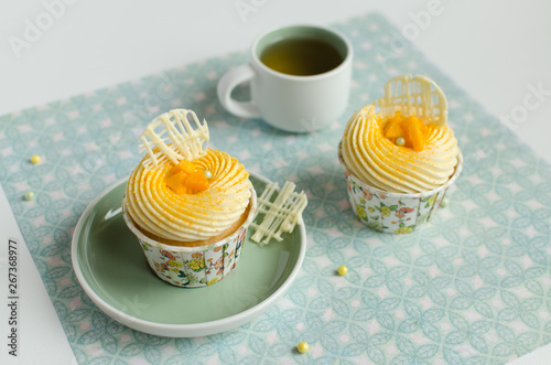 Tropical cupcakes decorated with piece of fresh mango and chocolate elements with a cup of green tea on green background