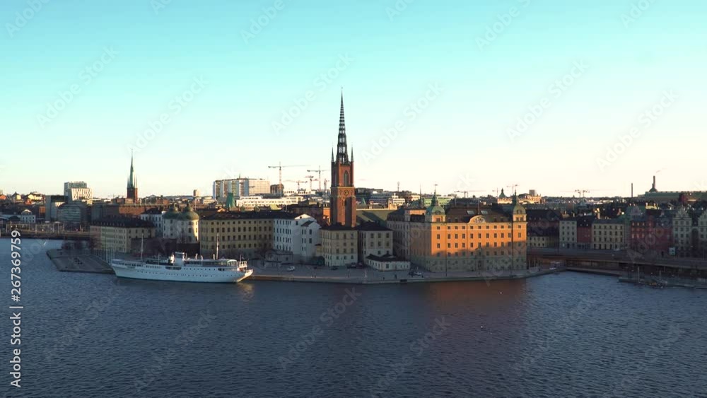 Sunrise panoramic scene across Stockholm cityscape & large cruise ship in harbour on calm blue sea. Shadowy waters & sunlight glow on building sides. Sunrise panoramic scene across Stockholm cityscape & large cruise ship in harbour on calm blue sea. Shadowy waters & sunlight glow on building sides.