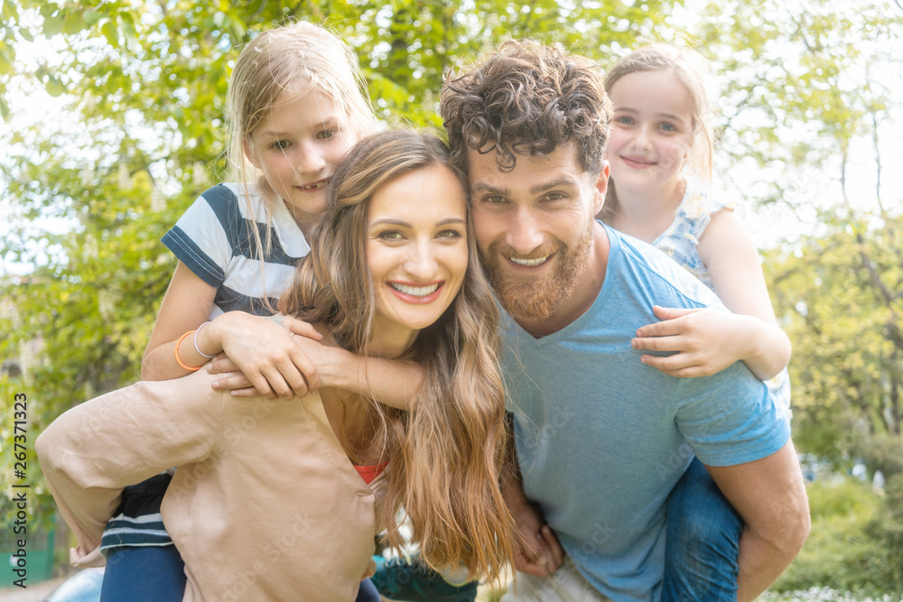 Family of four having fun and parents carrying the kids piggyback Family of four having fun and parents carrying the kids piggyback