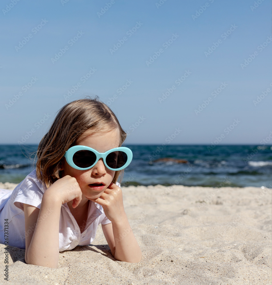 Funny little girl (7 years old) in sunglasses lies on the beach. Funny little girl (7 years old) in sunglasses lies on the beach.