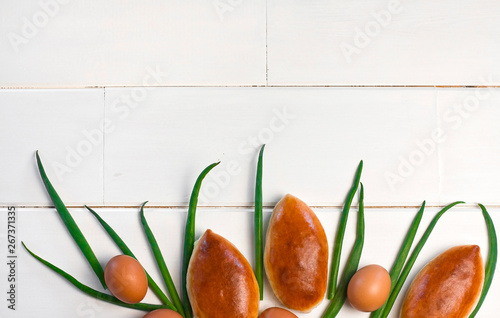  patties with egg and onions on a white wooden background. sweet cakes with filling. green onions photo