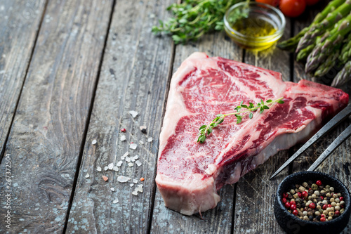 Raw T-bone Steak with fresh herbs and oil on dark wooden background