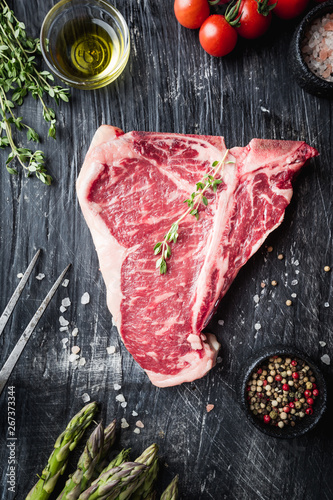 Raw T-bone Steak with fresh herbs and oil on black background, top view
