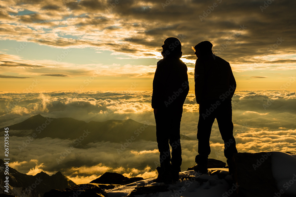 Friends above clouds in alpine mountains watching sunset from the summit, France / Italy border, Mont Blanc area