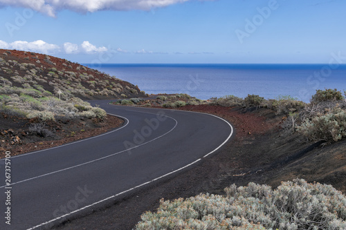 Asphalt road crossing volcanic area, with Atlantic ocean and blue sky background, La Restinga, El Hierro, Canary islands, Spain