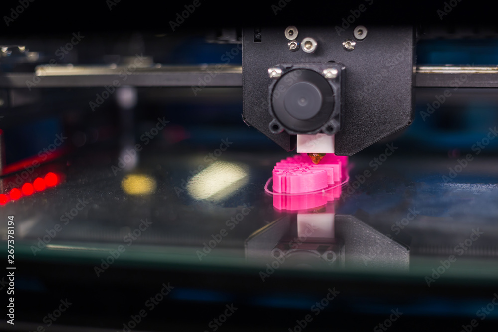Print head of 3D printer machine printing plastic model of pink fish skeleton at modern scifi technology exhibition. 3D printing, 4.0 industrial revolution and futuristic concept