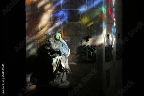 Glare from sunlight passing through the stained glass windows, paint the interior of the church and the sculpture of the Madonna and Child (Saint-Malo, France)