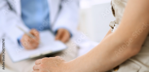Doctor and patient talking. Physician at work in hospital while writing up medication history records form on clipboard near sitting woman. Healthcare and medicine concepts