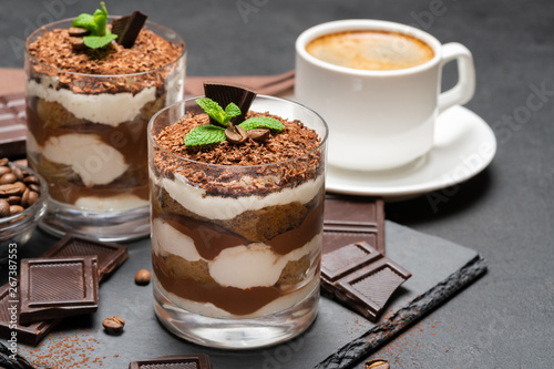 Classic tiramisu dessert in a glass and cup of coffee on dark concrete background