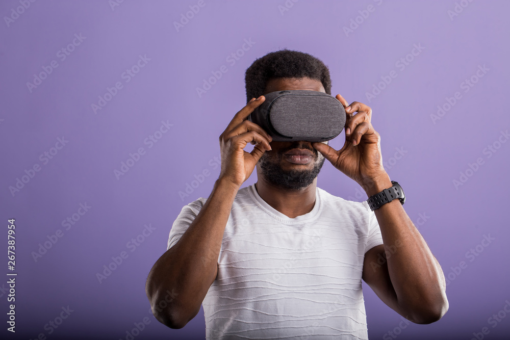 Handsome young African man in VR headset standing against purple background Handsome young African man in VR headset standing against purple background
