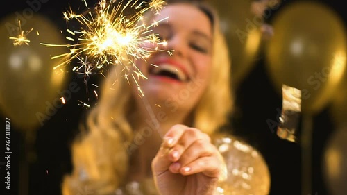 Pretty blond female waving bengal light under falling confetti on party, prom photo