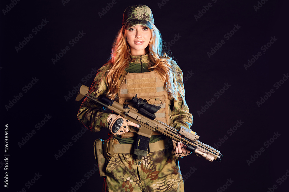 Female soldier in military camouflage uniform and cap holding sniper rifle over black background with smoky clouds Female soldier in military camouflage uniform and cap holding sniper rifle over black background with smoky clouds
