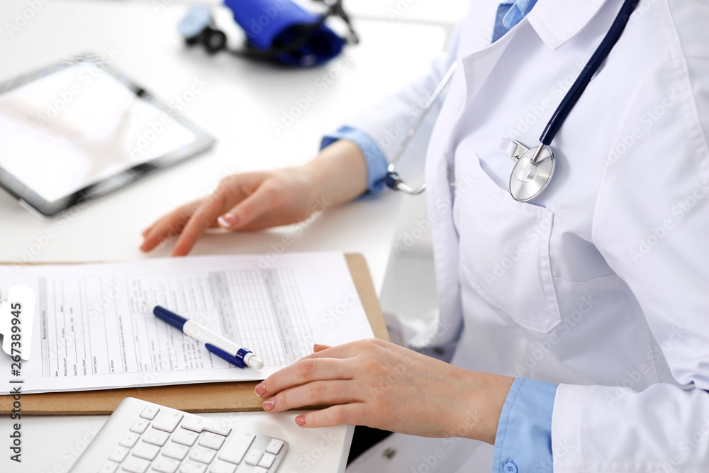 Doctor working table. Woman physician using tablet computer while sitting in hospital office close-up. Healthcare, insurance and medicine concept Doctor working table. Woman physician using tablet computer while sitting in hospital office close-up. Healthcare, insurance and medicine concept