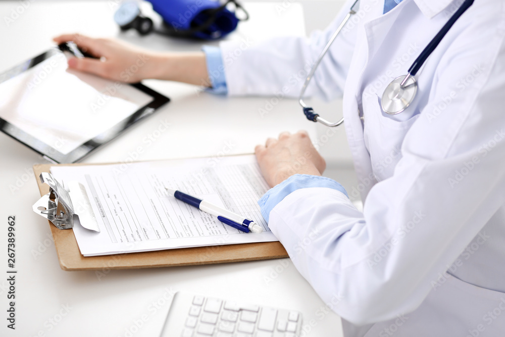 Doctor working table. Woman physician using tablet computer while sitting in hospital office close-up. Healthcare, insurance and medicine concept Doctor working table. Woman physician using tablet computer while sitting in hospital office close-up. Healthcare, insurance and medicine concept