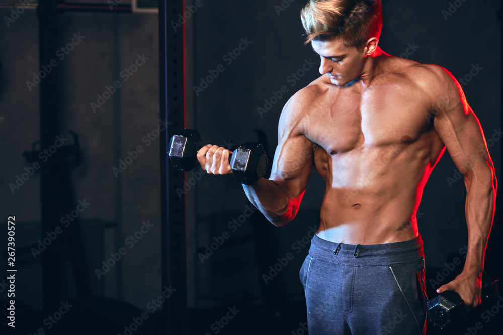 Caucasian man working out in gym doing exercises with dumbbells at triceps, strong male naked torso, highly defined muscles, six-packs slim trained body in dark gym