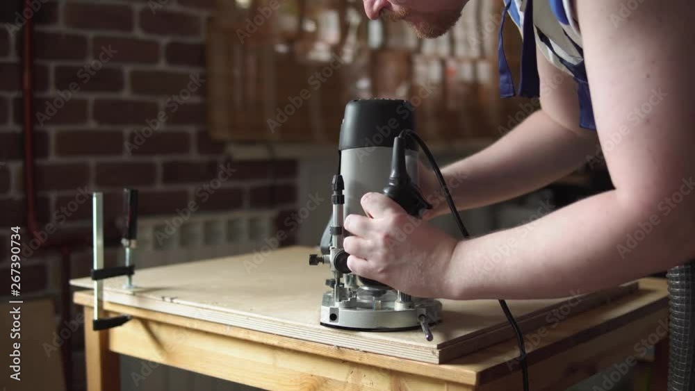 Blond carpenter works with modern handheld plunge router with dust ...