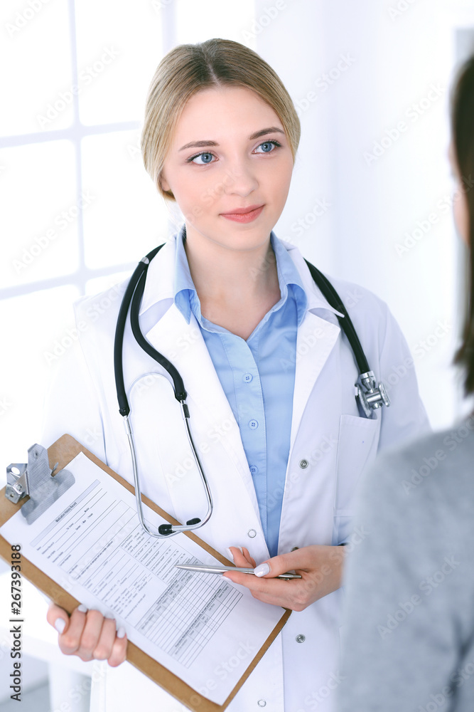 Young woman doctor and patient looking at medication history records while standing straight in hospital Blue colored blouse of therapist looks good. Medicine and healthcare concept Young woman doctor and patient looking at medication history records while standing straight in hospital Blue colored blouse of therapist looks good. Medicine and healthcare concept