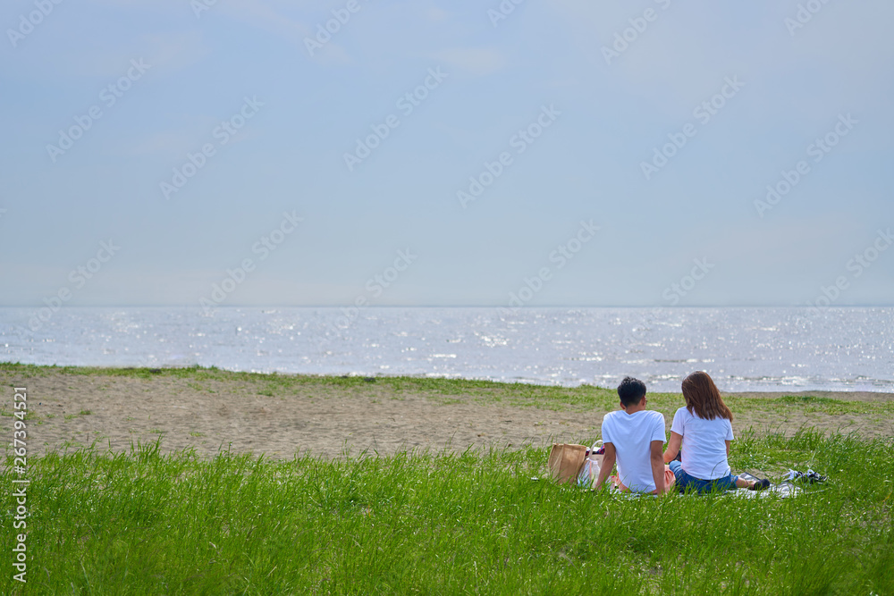 海岸で芝生の上に座る若いカップル、爽やかな夏の海。