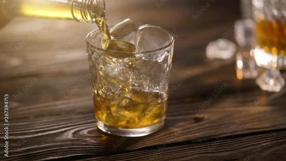 Bartender pouring whisky from bottle in to glass on rustic wooden table Bartender pouring whisky from bottle in to glass on rustic wooden table