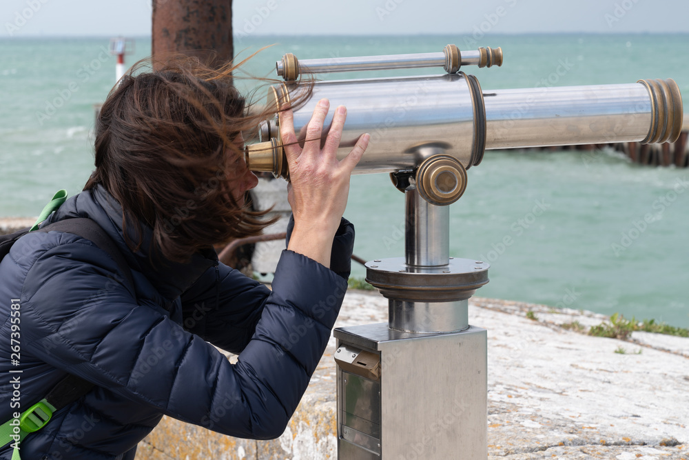 Woman brunette looking through coin operated binoculars at seaside ocean  beach Stock Photo | Adobe Stock