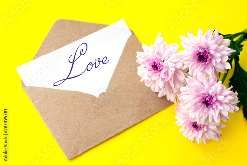 Love envelope and letter with written word love with pink flowers on bright yellow bacground.