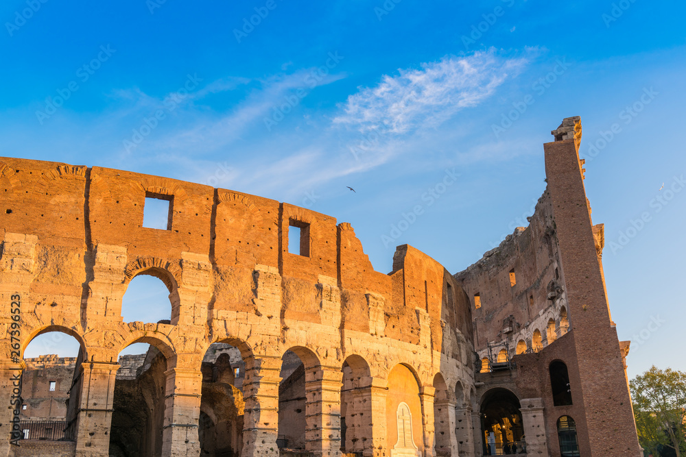 The Colosseum in Rome at golden sunrise with blue sky, Italy