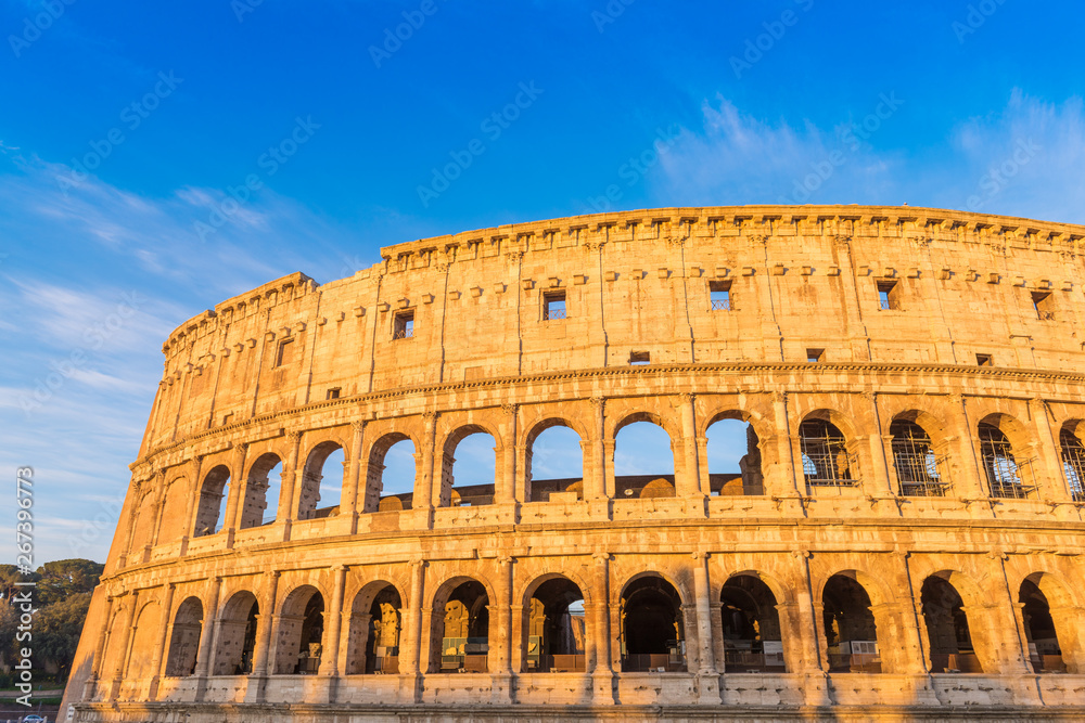 The Colosseum in Rome at golden sunrise with blue sky, Italy