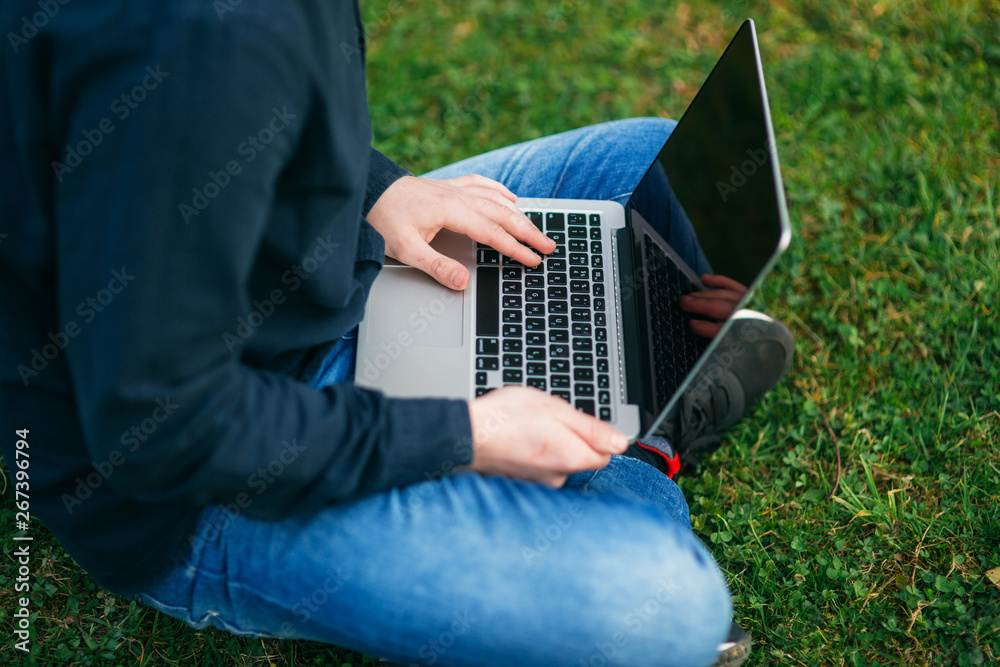 Mid selection of Young man sitting on the grass in the park and work on laptop Mid selection of Young man sitting on the grass in the park and work on laptop