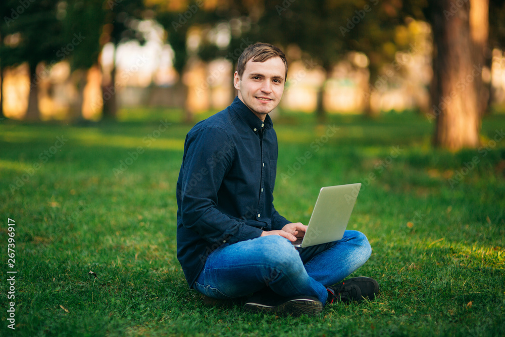 Young man sitting on the grass in the park and work on laptop Young man sitting on the grass in the park and work on laptop