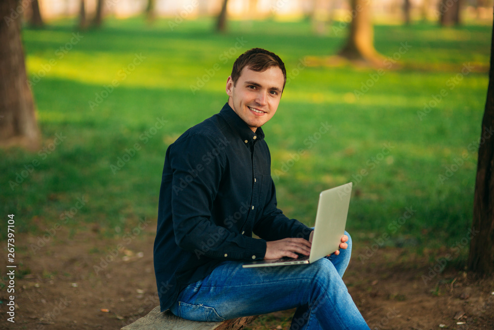 Programmer working in the park on laptop. Man sitting on bench