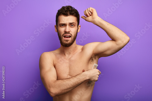 Handsome muscular naked man waxing his armpit, he doesn't like this procedure, painful process of getting rid of unnecessary hairs