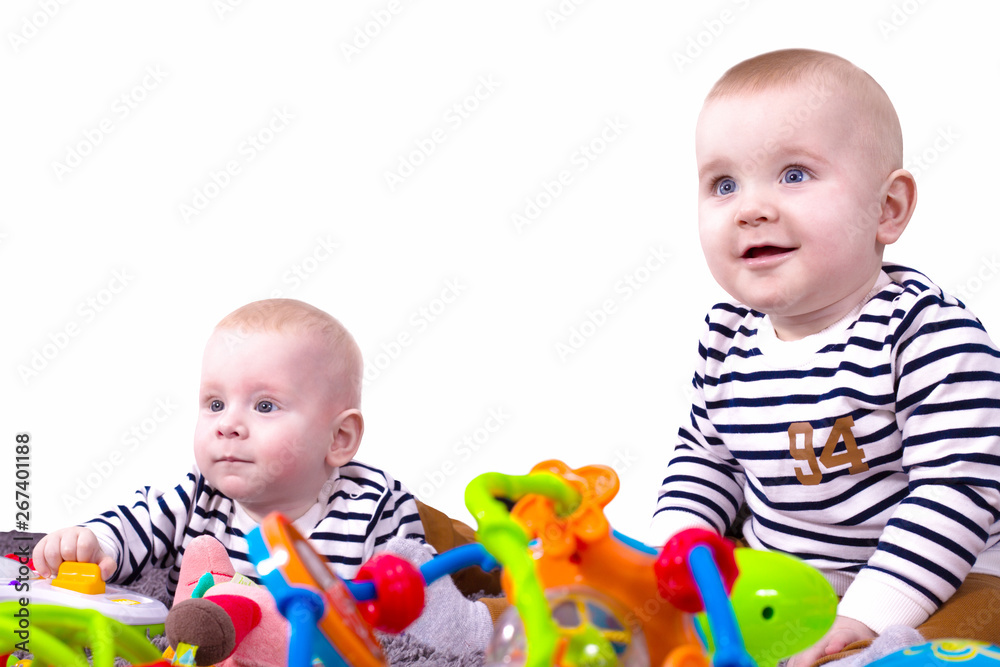 Adorable non-identical twins, also known as fraternal twins or dizygotic twins play with toys isolated on white background. Two happy boys, one sitting and one lying. Pretty toddlers. Adorable non-identical twins, also known as fraternal twins or dizygotic twins play with toys isolated on white background. Two happy boys, one sitting and one lying. Pretty toddlers.