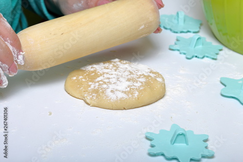 A woman rolls dough for making marshmallow sandwiches with a rolling pin. Nearby are forms for applying ornament on the dough.
