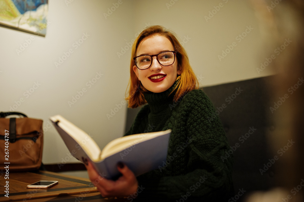 Cheerful young beautiful redhaired woman in glasses, wear on green warm wool sweater, sitting at cafe and using her notebook. Cheerful young beautiful redhaired woman in glasses, wear on green warm wool sweater, sitting at cafe and using her notebook.