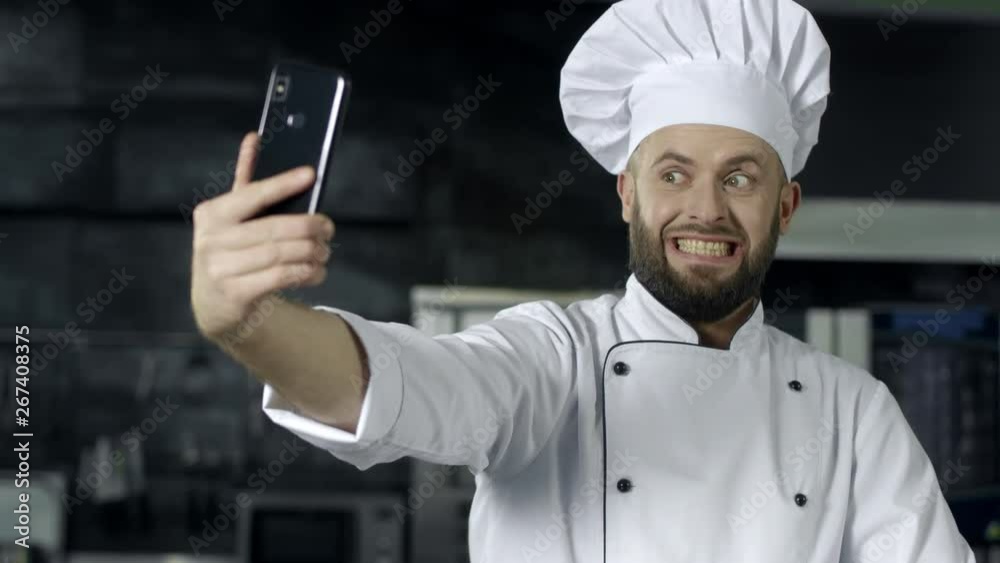 Professional chef posing at kitchen. Chef making selfie photo with mobile phone