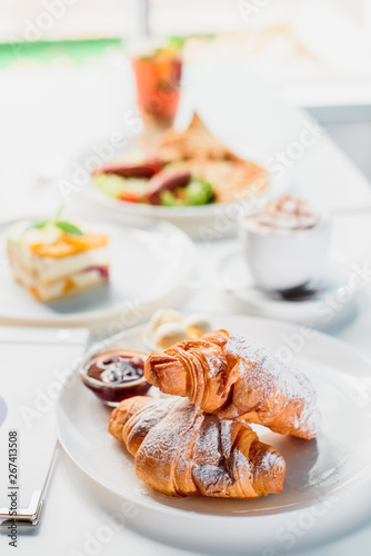Beautiful fresh French croissants with jam on a white plate on a light background in the restaurant. Close-up. Space