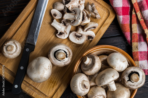 Fresh champignon mushrooms on a cutting board and on a black rustic background.