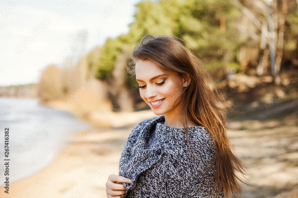 Natural beauty an attractive cute young girl, a portrait in a warm sweater on the river bank in early spring, a walk through the forest in nature - obrazy, fototapety, plakaty 
