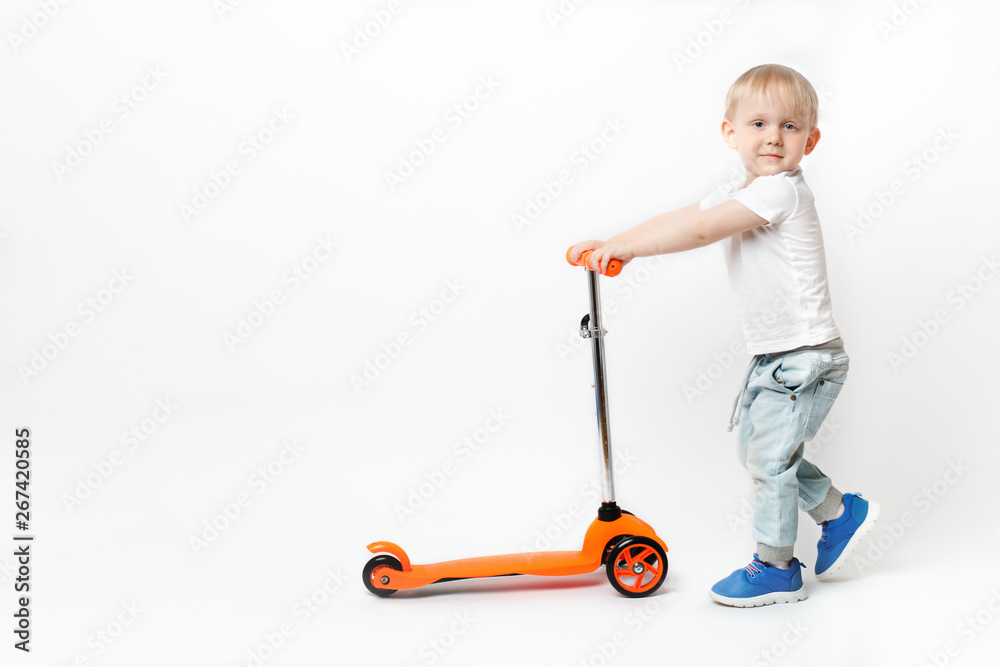 Toddler child rolls orange bright scooter by the handles on a white background. Toddler child rolls orange bright scooter by the handles on a white background.
