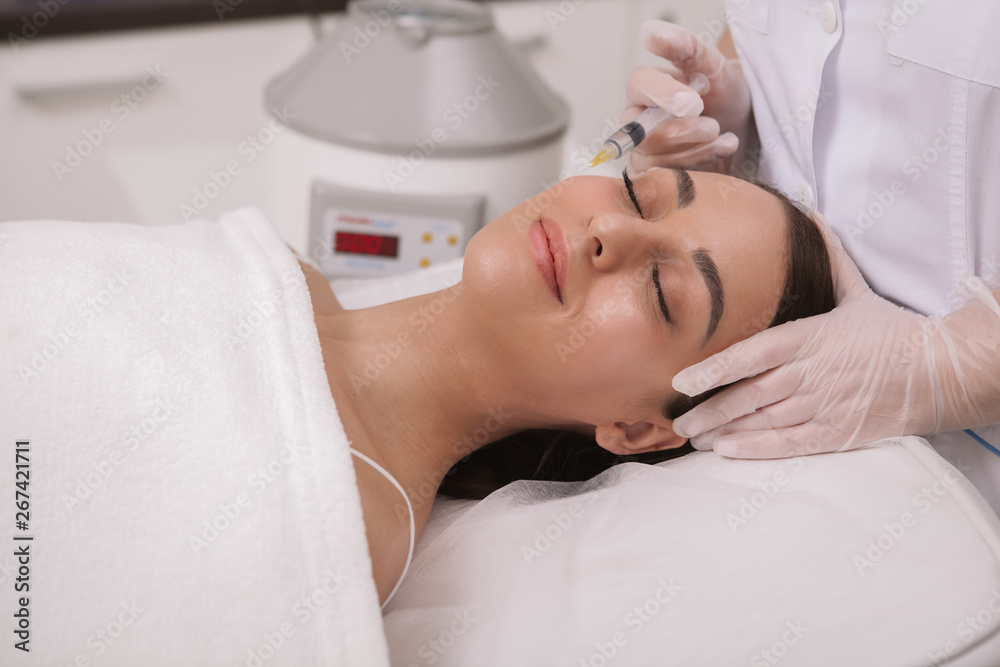 Lovely relaxed woman receiving facial hyaluronic acid injections by professional cosmetologist. Beauticul woman getting anti-aging filler injections at beauty salon. Anti-wrinkles concept