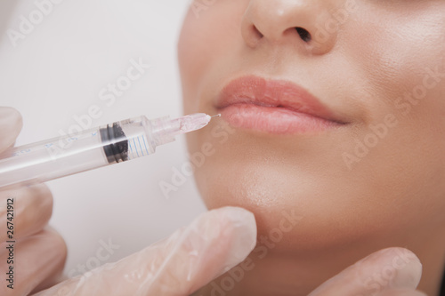 Cropped close up of a woman with beautiful sexy lips getting lip augmentation at cosmetology clinic. Beautician using syringe, performing lip injections for female client. Full lips concept