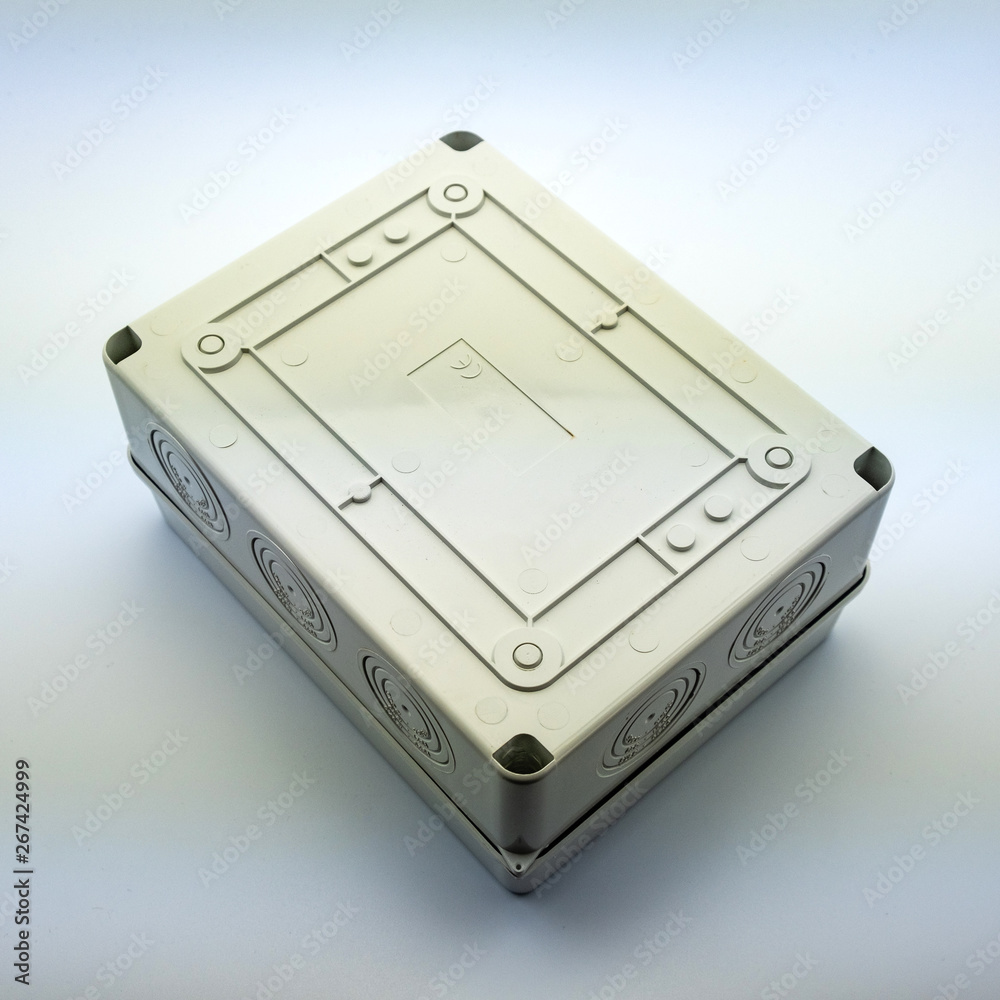 Obraz premium Plastic gray plastic electrical installation junction box on a white background. Electric switchboard on the white wall of a factory.