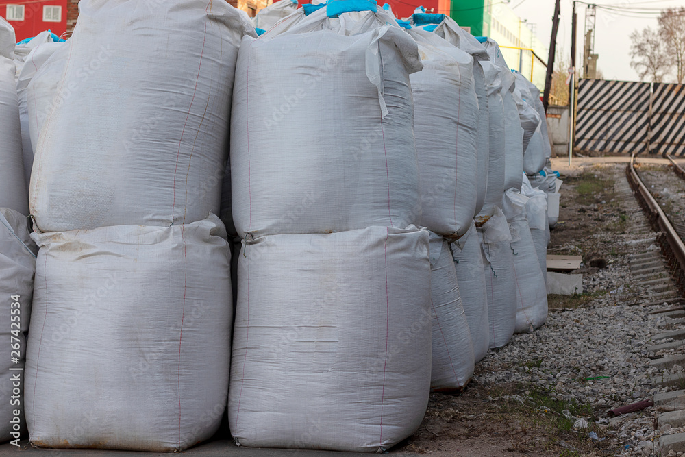 Large white bags of salt lie on the street. Industrial fertilizers are stored in bags in a heap.