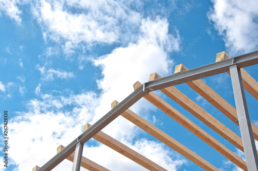 Metal frame of the new building against the blue sky with clouds. Metal frame of the building for further insulation. Wood beams and metal frame of the new building. Metal frame of the new building against the blue sky with clouds. Metal frame of the building for further insulation. Wood beams and metal frame of the new building.