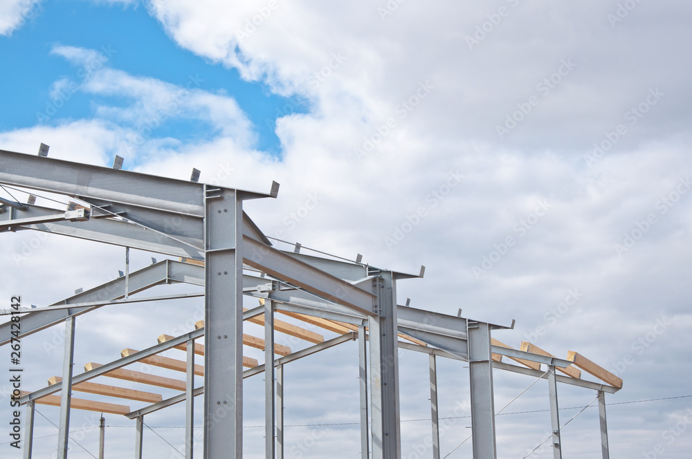 Metal frame of the new building against the blue sky with clouds. Metal frame of the building for further insulation. Wood beams and metal frame of the new building. Metal frame of the new building against the blue sky with clouds. Metal frame of the building for further insulation. Wood beams and metal frame of the new building.