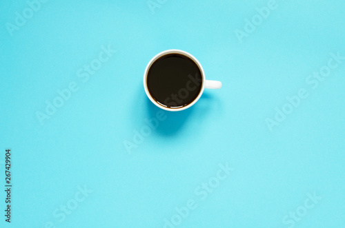 Flat lay cup of black coffee on blue background. Minimalistic food concept.
